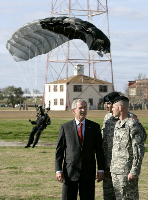President George W. Bush speaks with U.S. Army Colonel Mike Linnington, center, and Sgt. 1st Class Mike Hertig, right, as he watches paratroopers from the U.S. Army Silver Wings Command exhibition team land Thursday, Jan. 11, 2006, during a demonstration of airborne infantry training at Fort Benning, Ga. White House photo by Eric Draper