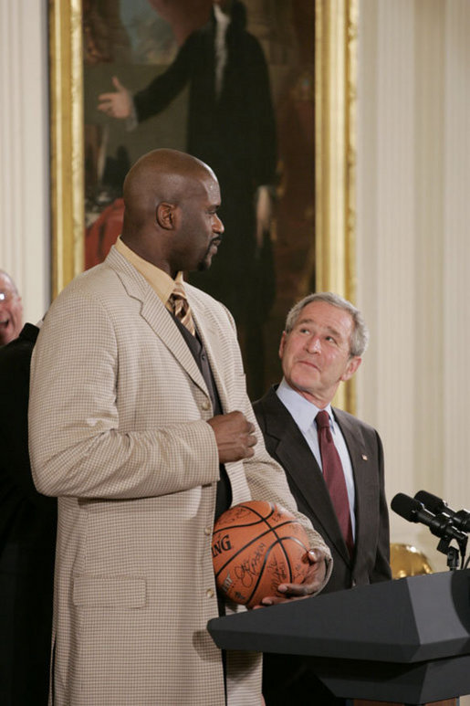 President George W. Bush looks up as he prepares to receive an autographed ball from Shaquille O'Neal Tuesday, Feb. 27, 2007, as the 2006 NBA champions visited the White House. The President told the East Room audience he was most impressed by the Heat's work in their Miami community and added, "I mean, I'm in awe of their athletic skills. Standing next to Shaq is an awe-inspiring experience." White House photo by Paul Morse