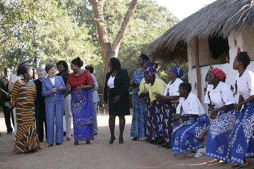 Mrs. Laura Bush walks with Zambian First Lady Mrs. Maureen Manawasa, center right, Thursday, June 28, 2007, at the Flame Community Center in Lusaka, Zambia. They are greeted in song by members of the WORTH Tufune Women's Group. The WORTH group trains women in literacy, group savings, peer lending and the development of small business. White House photo by Shealah Craighead