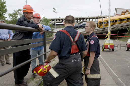 President George W. Bush, accompanied by Gary Babineau of Blaine, Minn., right, talks with fire and rescue personnel during a tour of the Interstate 35W bridge collapse scene in Minneapolis, Saturday, Aug. 4, 2007. Babineau, who was on the bridge during the collapse, helped rescue schoolchildren from their bus, seen in background, to safety. White House photo by Chris Greenberg