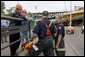 President George W. Bush, accompanied by Gary Babineau of Blaine, Minn., right, talks with fire and rescue personnel during a tour of the Interstate 35W bridge collapse scene in Minneapolis, Saturday, Aug. 4, 2007. Babineau, who was on the bridge during the collapse, helped rescue schoolchildren from their bus, seen in background, to safety. White House photo by Chris Greenberg