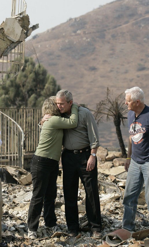 President George W. Bush hugs Kendra Jeffcoat as her husband Jay stands by in the midst of the charred rubble of their Rancho Bernardo, California home. The President met the couple during his visit Thursday, Oct. 25, 2007, to the Southern California areas ravaged by recent wildfires. White House photo by Eric Draper