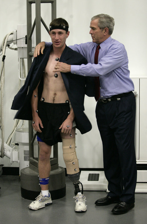 President George W. Bush offers his jacket to U.S. Army PFC Nicholas Clark of Seattle, Wash., during his visit Thursday, Nov. 8, 2007 to the Gait Lab at the Center for The Intrepid at the Brooke Army Medical Center in San Antonio, Texas. PFC Clark, who lost a leg while serving in Afghanistan in 2007, is participating in a demonstration wearing retro-reflective markers to measure his body movements under infra-red cameras. White House photo by Eric Draper