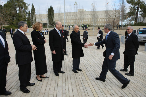 With Prime Minister Ehud Olmert looking on, President George W. Bush reaches out to Israel's President Shimon Peres Friday, Jan. 11, 2008, as he arrives at Yad Vashem , the Holocaust Museum, in Jerusalem. White House photo by Eric Draper