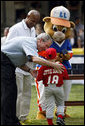 President George W. Bush presents Angel Tavarez, of the Cramer Hill Little League Red Sox from Camden, New Jersey, with a baseball Monday, June 30, 2008, following the opening game of the 2008 Tee Ball on the South Lawn. President Bush is joined on the field by Roberto Clemente, Jr. and Dugout, the Little League mascot. White House photo by Eric Draper