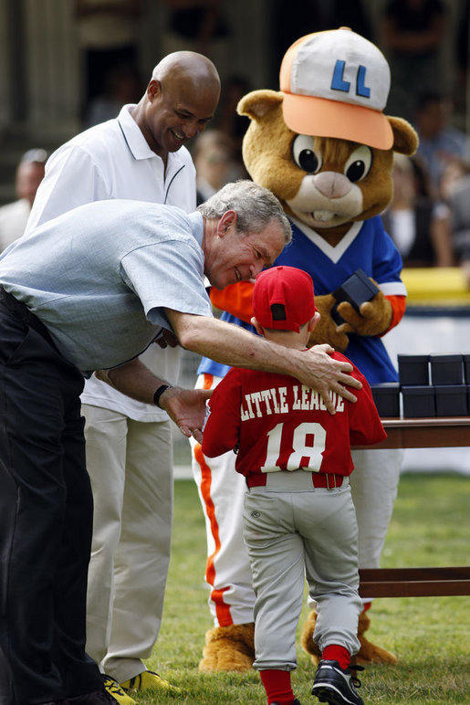 President George W. Bush presents Angel Tavarez, of the Cramer Hill Little League Red Sox from Camden, New Jersey, with a baseball Monday, June 30, 2008, following the opening game of the 2008 Tee Ball on the South Lawn. President Bush is joined on the field by Roberto Clemente, Jr. and Dugout, the Little League mascot. White House photo by Eric Draper