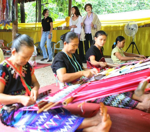 Mrs. Laura Bush and daughter Ms. Barbara Bush try on shawls created by weavers carrying on the traditional Karen ethnic craft at the Mae La Refugee Camp at Mae Sot, Thailand. In her August 7, 2008 comments, Mrs. Bush pointed out that the weavings are done to help generate money for the refugees and can be purchased via the Internet through consortiums that work with women at the camp. The camp houses at least 39,000 refugees waiting for a safe time to return to their home country. Many have decided the wait of 20 years has been too long and have immigrated to the United States and other countries. White House photo by Shealah Craighead