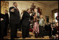 President George W. Bush is joined by two children on stage in the East Room of the White House as he thanks members of the musical group Sweet Heaven Kings, Monday, Dec. 8, 2008, during the Children's Holiday Reception and Performance. White House photo by Eric Draper