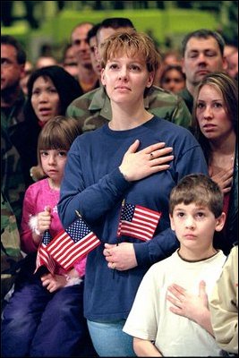 Family members of Air Force personnel place their hands over their hearts at Elmendorf Air Force Base in Anchorage, Alaska, Feb. 16, 2002. "I'm honored to be in a place where people understand the need for sacrifice and patriotism," said the President. "And I've come to Alaska to let you know that I'm proud of our United States military; that when I sent you into action, I knew you would not let this nation down."
