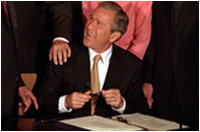 Surrounded by Senators and members of Congress who supported the legislation, President George W. Bush signs the tax bill on Thursday, June 7, 2001 in the East Room of the White House. 