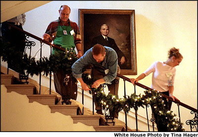 Under the watchful gaze of Harry S. Truman's portrait, volunteers Mike Bickley (left), David Padua (center) and Samantha Rutledge hang garland on the Grand Staircase, which leads from the Grand Foyer up to the President's residence. White House photo by Tina Hager.