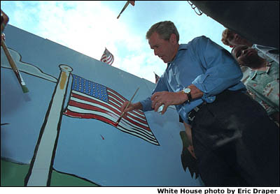As American flag throughout the neighborhood furled in the breeze, the President made a few waves of his own helping local children paint an American flag July 4, 2001. White House photo by Eric Draper