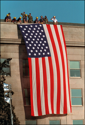 One day after terrorists used commercial airplanes to destroy the World Trade Center Towers and attack the Pentagon, firefighters take a moment to unfurl the flag over the scarred stone as inspiration for fellow rescue workers searching through the debris Sept. 12