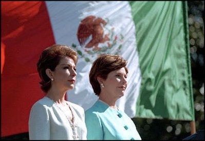 As a breeze unfurls the two nation's flags, Laura Bush and Martha Sahagun de Fox stand at attention.