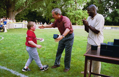 President George W. Bush presents autographed baseballs to Tee Ball players after their game on the South Lawn July 27, 2003. Darrell Green, the Guest Commissioner, is to the right of the President. 