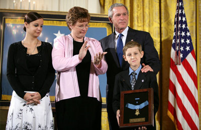 President George W. Bush places his hand on the shoulder of 11-year-old David Smith after he presented the young man with the Medal of Honor, awarded his father, Sgt. 1st Class Paul Smith, posthumously Monday during ceremonies at the White House. Joining David on stage are his step-sister Jessica and his mother, Birgit Smith. White House photo by Eric Draper