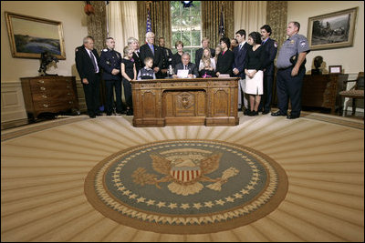President George W. Bush delivers a Live Radio Address surrounded by Mrs. Bush and families of victims of 911 in the Oval Office, Saturday, Sept. 11, 2004.