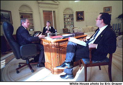 Working at his desk in the Oval Office, President Bush looks over one of the countless versions of the speech with Counselor Karen Hughes and Speechwriter Mike Gerson, Thursday, Jan. 24. The slow process involves dozens of people and can last many weeks. White House photo by Eric Draper.