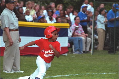 A player rounds first base as Transportation Secretary Norman Mineta umpires the first base line during the second Tee Ball game on the South Lawn on Sunday, June 3, 2001.