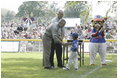 President George W. Bush and Honorary Commissioner Cal Ripken present a little leaguer with a warm congratulations and an autographed baseball after playing the last game of the 2003 White House South Lawn Tee Ball season Sunday, Sept. 7, 2003.