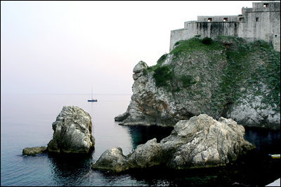 A solitary sailboat drifts along the Adriatic coast below the city wall of the Old City of Dubrovnik, Croatia, Saturday, May 6, 2006.