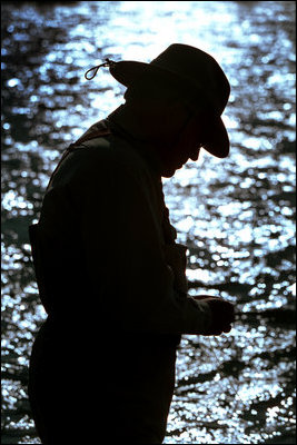 Silhouetted by the sunlight's reflection on the Snake River, Vice President Dick Cheney prepares his line before an afternoon of fishing.