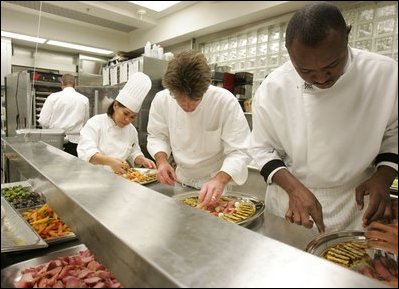 White House Executive Chef, Cristeta " Cris" Comerford, background-left in chef's hat, helps prepare trays of food, Wednesday, Nov. 2, 2005, in the White House kitchen, in preparations for the official dinner for the Prince of Wales and Duchess of Cornwall.